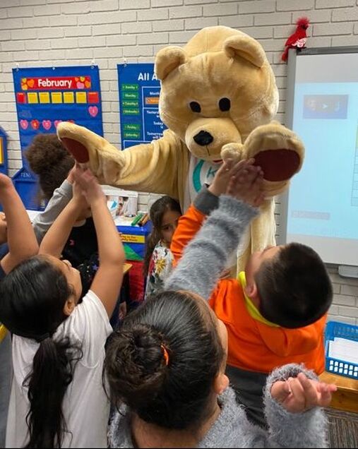 K/H bear giving high-fives to students in classroom